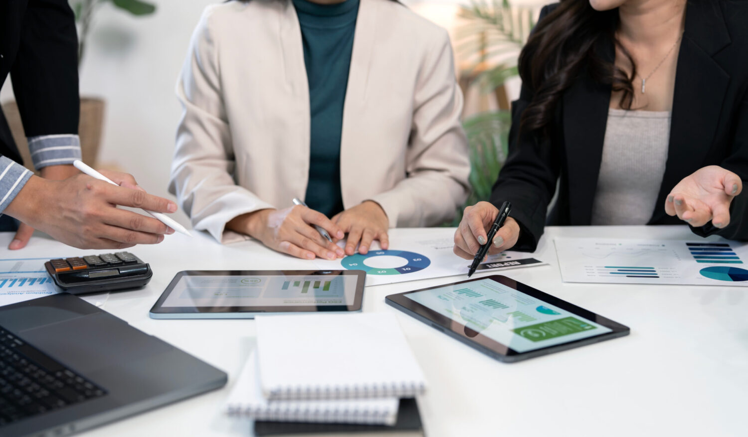 Business professionals collaborate, analyze financial data, and discuss marketing strategy using digital tablets and documents in a modern office meeting.
